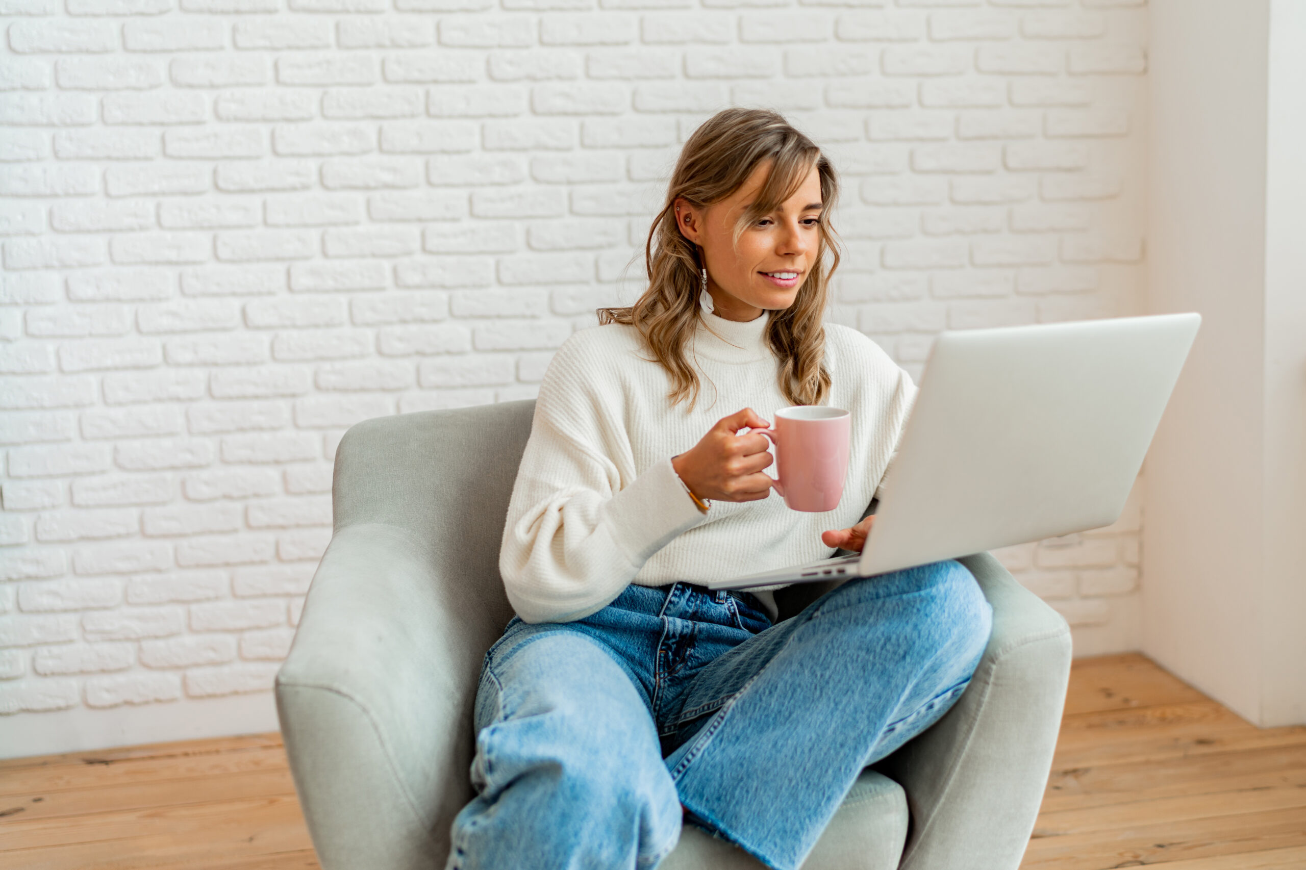 Smiling woman with blond wavy hairs sitting on sofa at home wor